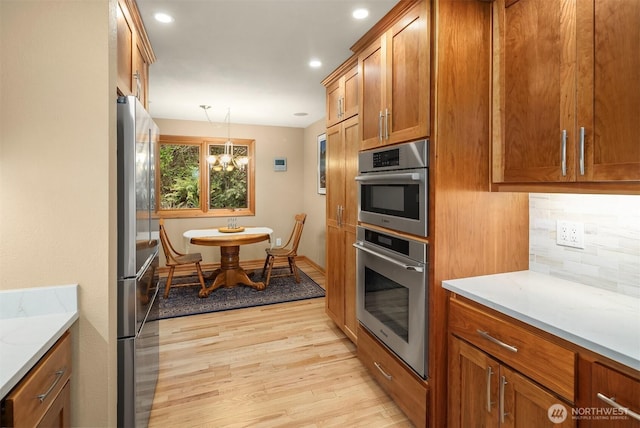 kitchen featuring light wood-style floors, appliances with stainless steel finishes, decorative backsplash, and brown cabinets