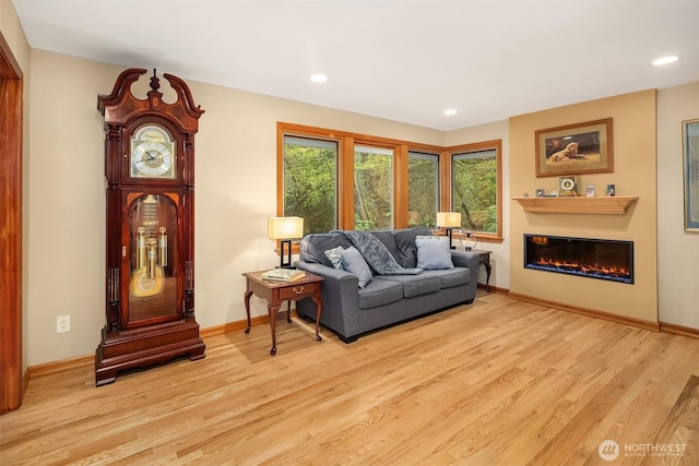 living room with a glass covered fireplace, baseboards, recessed lighting, and wood finished floors