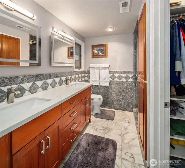 bathroom with visible vents, a sink, marble finish floor, and tile walls