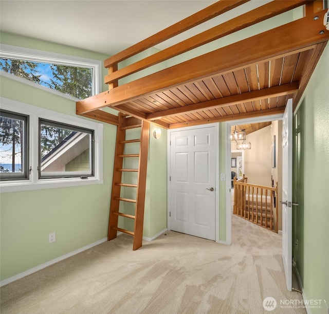 unfurnished bedroom featuring carpet floors, baseboards, wooden ceiling, and beam ceiling