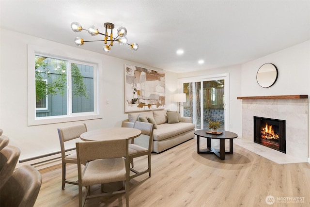 living area featuring baseboard heating, a fireplace, a chandelier, light wood-style flooring, and recessed lighting