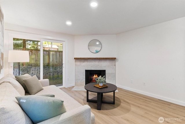 living area with recessed lighting, baseboards, a tiled fireplace, and light wood-type flooring