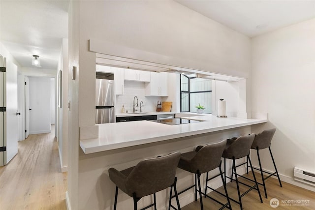 kitchen with white cabinets, freestanding refrigerator, a kitchen bar, and light wood-style flooring