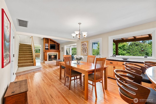 dining space featuring plenty of natural light, light wood-style flooring, stairs, a lit fireplace, and vaulted ceiling