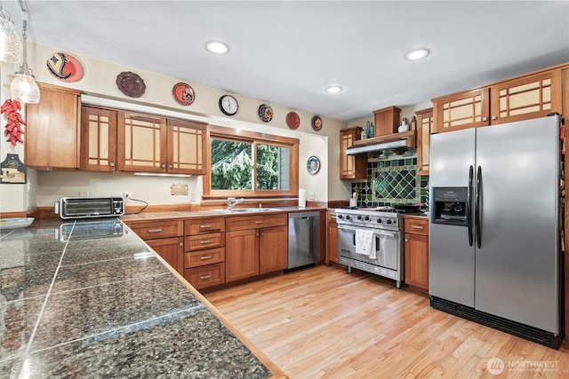 kitchen with stainless steel appliances, tile countertops, a sink, brown cabinets, and under cabinet range hood