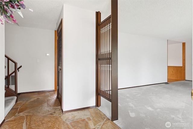 interior space with carpet floors, a textured ceiling, stone finish floor, stairs, and baseboards