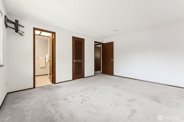 unfurnished bedroom with carpet flooring, a textured ceiling, baseboards, and ensuite bath