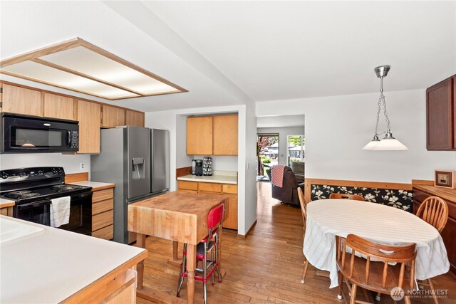 kitchen featuring light brown cabinetry, light countertops, light wood-style flooring, pendant lighting, and black appliances