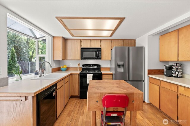 kitchen with light wood-type flooring, a sink, black appliances, and light countertops