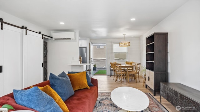 living room featuring stacked washer and dryer, light wood-type flooring, recessed lighting, a barn door, and a wall unit AC