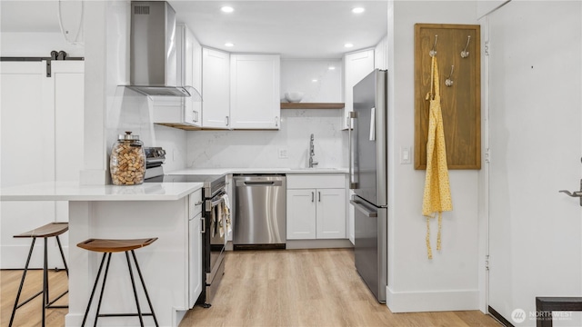 kitchen with a breakfast bar, wall chimney exhaust hood, a sink, light wood-style flooring, and appliances with stainless steel finishes