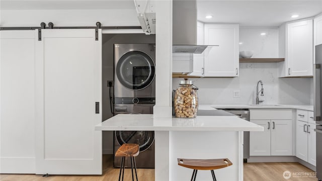 kitchen featuring stacked washer / dryer, a breakfast bar, light wood-type flooring, white cabinets, and a sink