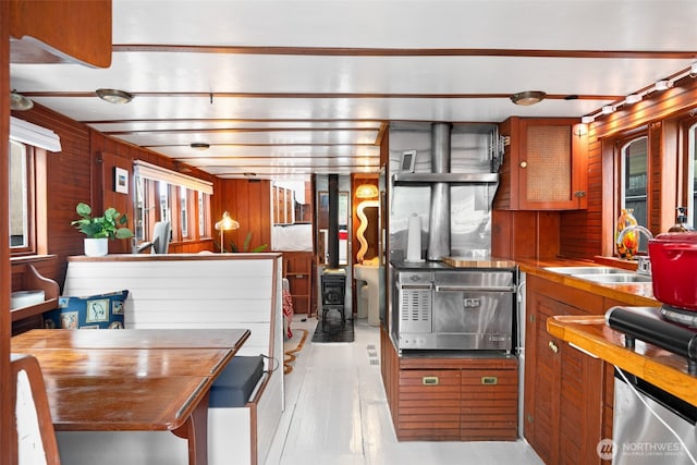 kitchen featuring a sink, brown cabinetry, a wood stove, and wooden walls