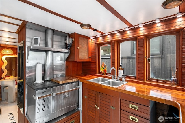 kitchen with brown cabinets, wood walls, butcher block counters, and a sink