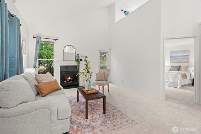 living room featuring baseboards, carpet flooring, a warm lit fireplace, and high vaulted ceiling