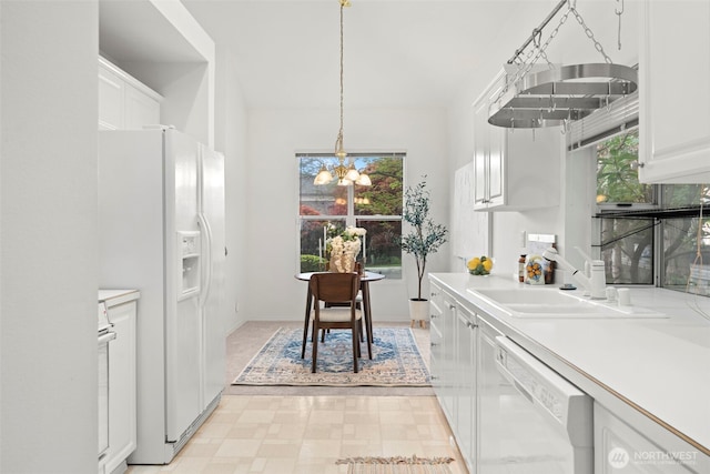 kitchen with white appliances, light countertops, white cabinetry, a sink, and a notable chandelier