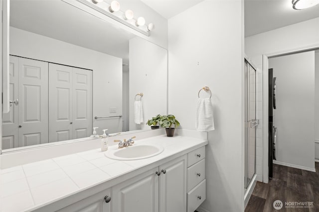 bathroom featuring a stall shower, wood finished floors, vanity, baseboards, and a closet