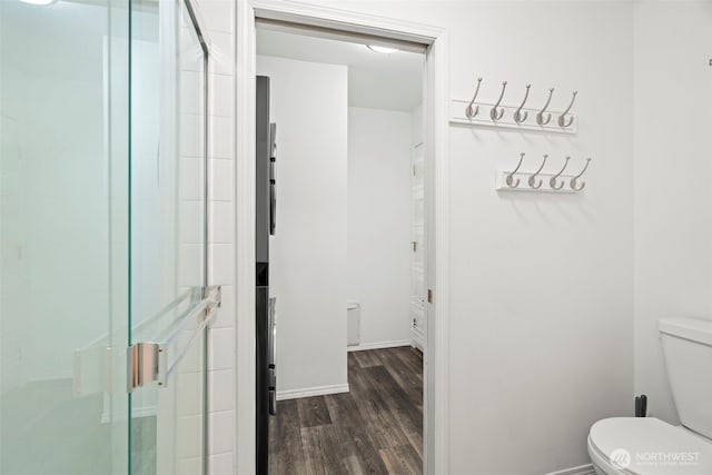 bathroom featuring baseboards, wood finished floors, toilet, and a shower stall