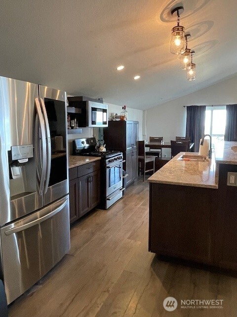 kitchen with recessed lighting, a sink, light wood-style flooring, appliances with stainless steel finishes, and vaulted ceiling