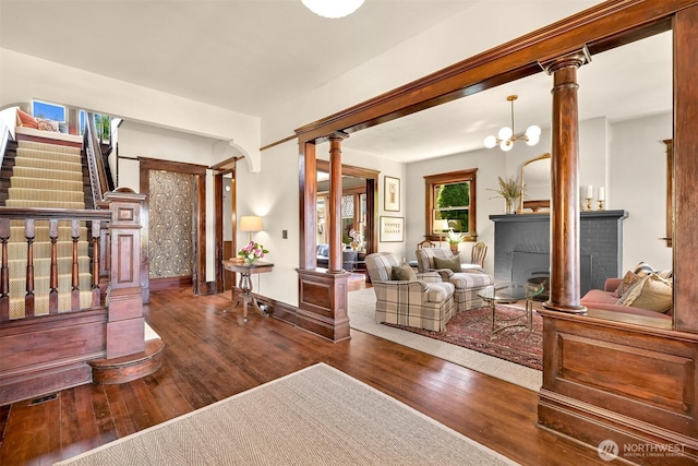 living area with a fireplace, baseboards, decorative columns, wood finished floors, and stairway