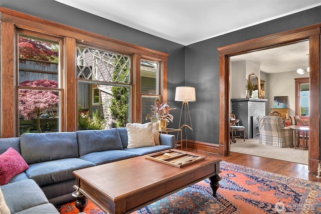 living area featuring baseboards, a brick fireplace, and wood finished floors