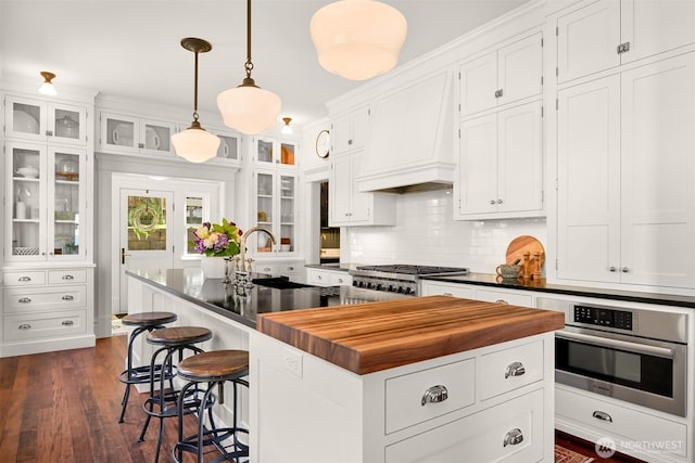 kitchen with oven, a sink, butcher block counters, white cabinetry, and an island with sink