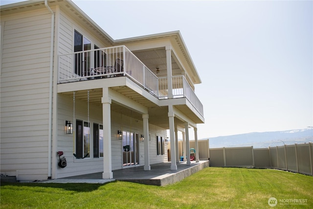 rear view of property with a lawn, fence, a mountain view, and a balcony