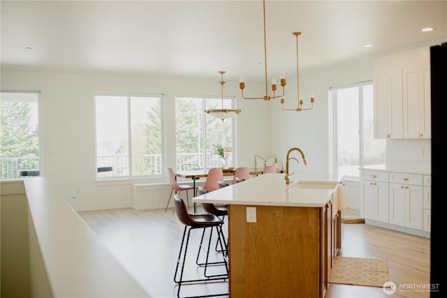 kitchen with a notable chandelier, a sink, a kitchen island with sink, a kitchen breakfast bar, and light countertops