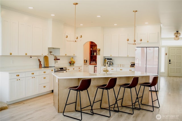 kitchen featuring freestanding refrigerator, electric stove, white cabinetry, arched walkways, and light wood-style flooring