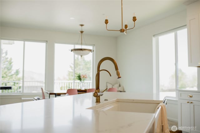 kitchen with a sink, pendant lighting, a notable chandelier, and light countertops