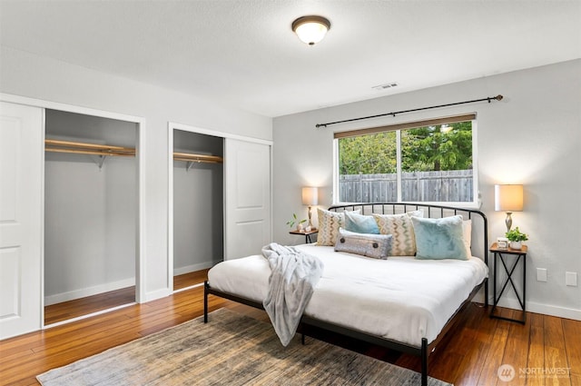 bedroom featuring visible vents, multiple closets, baseboards, and hardwood / wood-style flooring