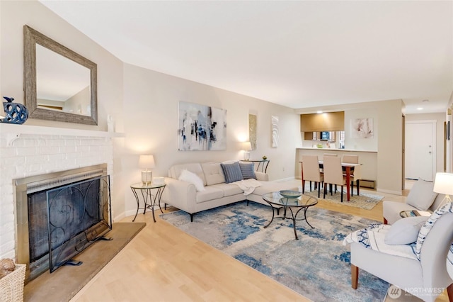 living room featuring a brick fireplace, baseboards, and wood finished floors