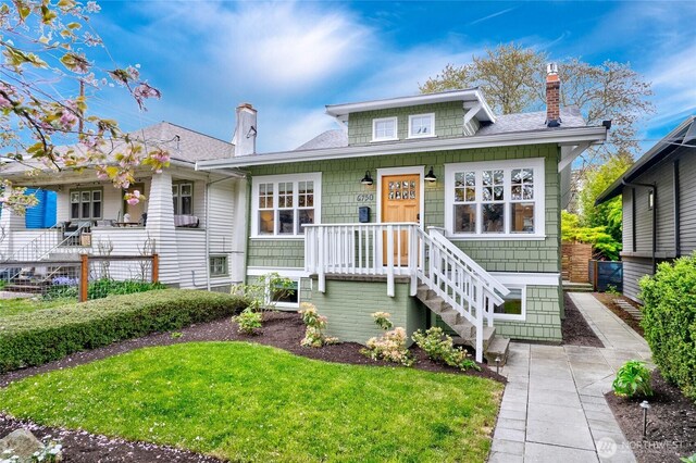 bungalow-style home with roof with shingles, fence, a front yard, and a chimney