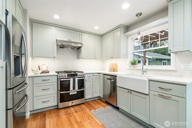 kitchen featuring decorative backsplash, light wood-style floors, under cabinet range hood, a sink, and stainless steel appliances