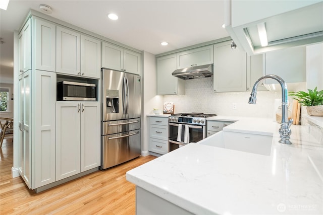 kitchen with a sink, light wood-style flooring, stainless steel appliances, decorative backsplash, and under cabinet range hood