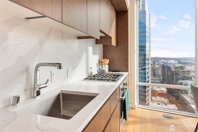 kitchen with decorative backsplash, wood finished floors, light stone countertops, modern cabinets, and a sink