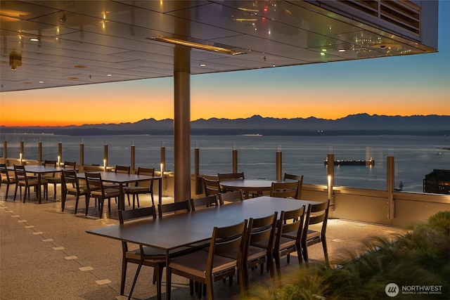 patio terrace at dusk featuring outdoor dining area and a water and mountain view