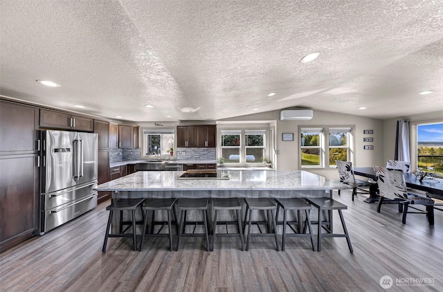 kitchen with appliances with stainless steel finishes, a wall mounted air conditioner, a kitchen breakfast bar, wood finished floors, and lofted ceiling