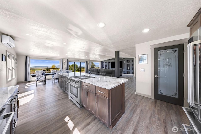 kitchen with dark brown cabinetry, stainless steel stove, open floor plan, an AC wall unit, and a textured ceiling