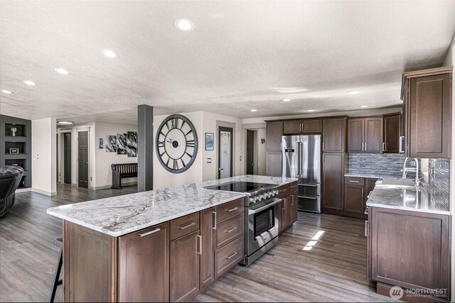 kitchen with a sink, a textured ceiling, a spacious island, and stainless steel appliances
