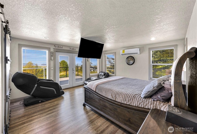 bedroom featuring wood finished floors, access to exterior, a textured ceiling, a wall unit AC, and french doors