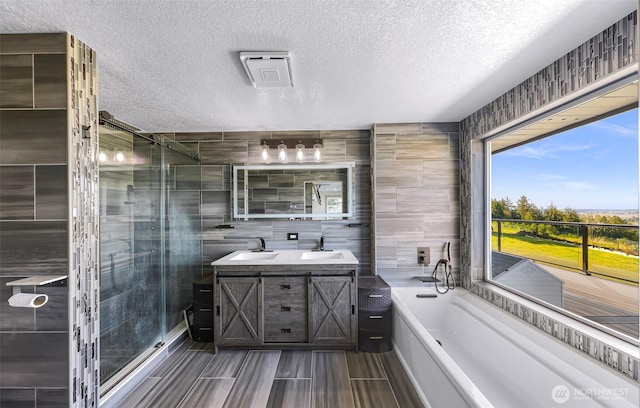 bathroom with a garden tub, double vanity, tile walls, a sink, and a stall shower