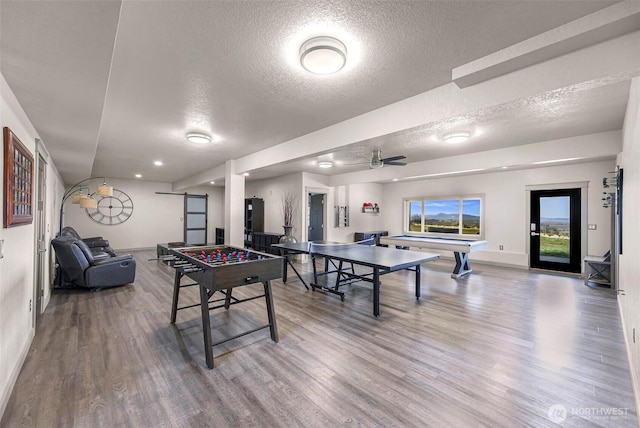 playroom with a barn door, ceiling fan, a textured ceiling, and wood finished floors