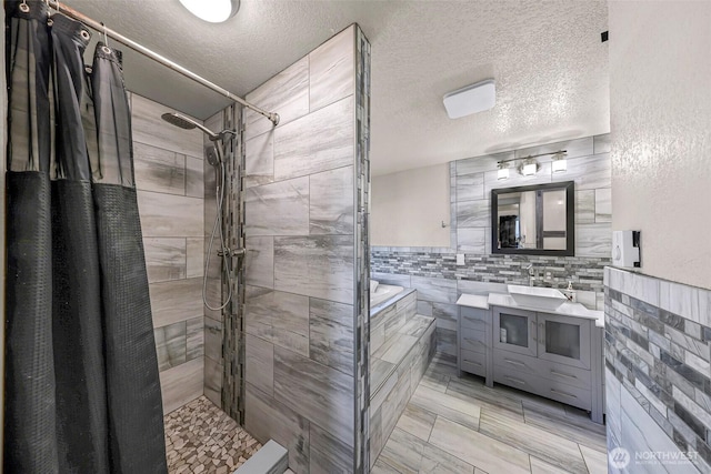 bathroom featuring vanity, a bath, a tile shower, and a textured ceiling