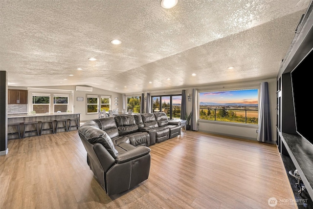 living room featuring light wood-style floors, a wall mounted air conditioner, a textured ceiling, recessed lighting, and lofted ceiling