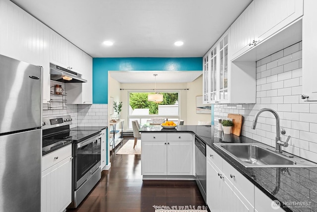 kitchen with a peninsula, under cabinet range hood, white cabinets, a sink, and stainless steel appliances