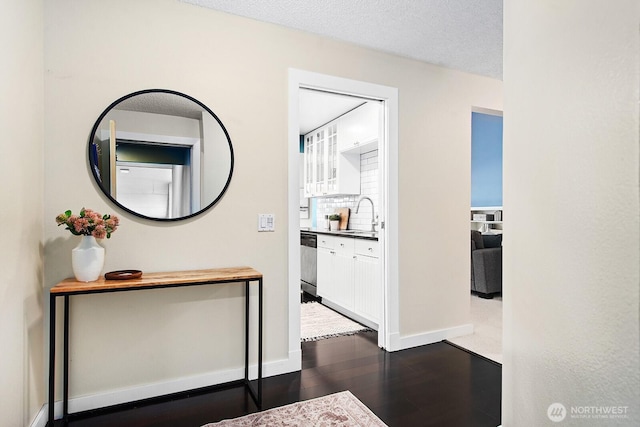 hallway featuring a textured ceiling, baseboards, dark wood-style floors, and a sink