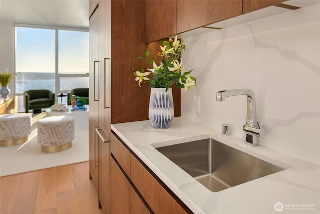 kitchen with a sink, light stone counters, brown cabinets, and light wood-style flooring