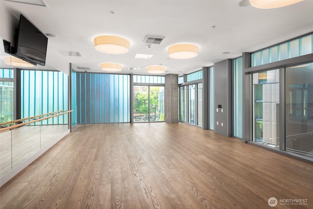 spare room with a wall of windows, wood finished floors, and visible vents