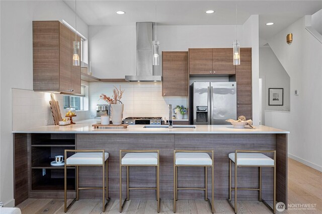 kitchen featuring modern cabinets, a kitchen breakfast bar, wall chimney range hood, stainless steel refrigerator with ice dispenser, and backsplash